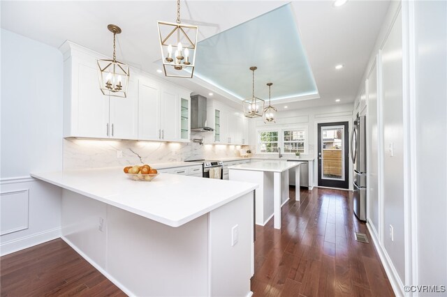 kitchen with white cabinets, a kitchen breakfast bar, kitchen peninsula, stainless steel appliances, and wall chimney exhaust hood