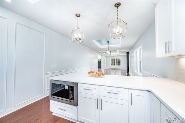 kitchen with stainless steel microwave, hanging light fixtures, white cabinetry, and dark hardwood / wood-style flooring