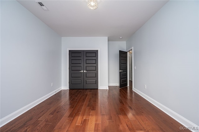 unfurnished bedroom featuring dark wood-type flooring, baseboards, visible vents, and a closet