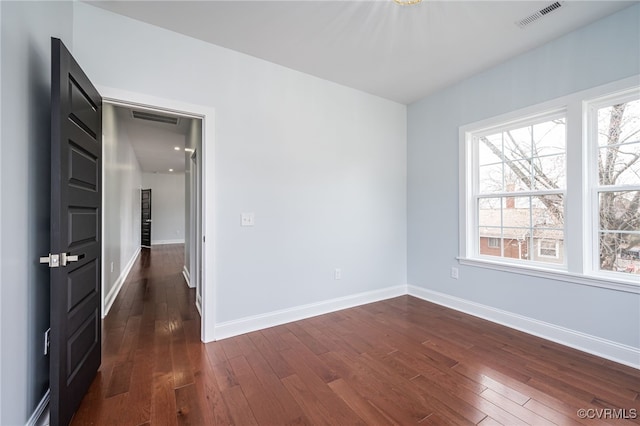 unfurnished room featuring baseboards, visible vents, and dark wood finished floors