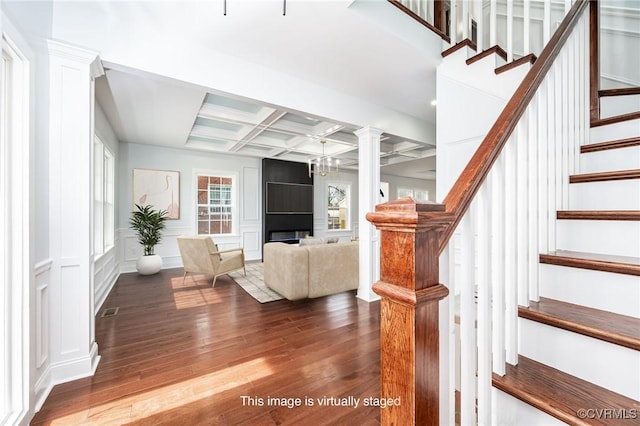 stairway with coffered ceiling, visible vents, beamed ceiling, a decorative wall, and hardwood / wood-style floors