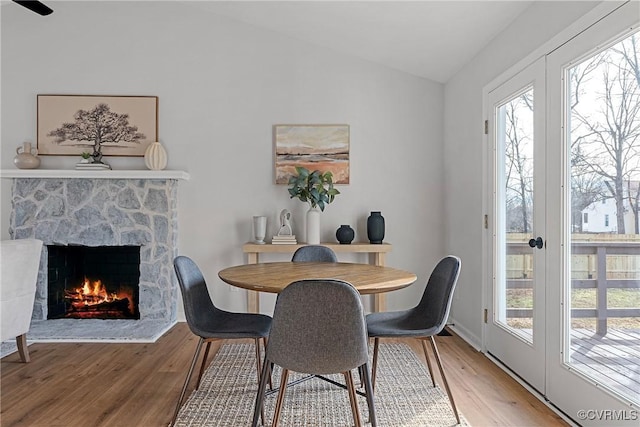 dining space featuring hardwood / wood-style flooring, a stone fireplace, and lofted ceiling