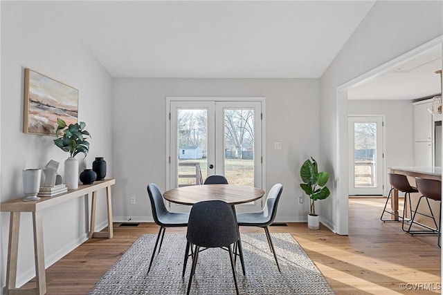 dining room featuring french doors, vaulted ceiling, and light hardwood / wood-style flooring