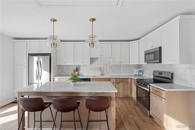 kitchen featuring appliances with stainless steel finishes, white cabinets, pendant lighting, a kitchen island, and light wood-type flooring