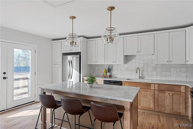 kitchen with a kitchen island, stainless steel refrigerator, light stone countertops, sink, and white cabinets