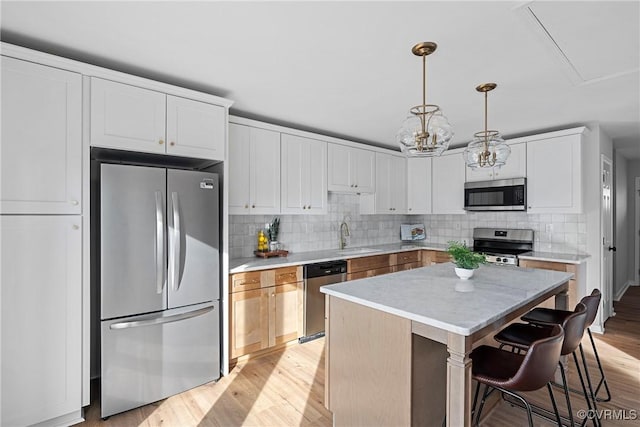 kitchen featuring appliances with stainless steel finishes, white cabinets, decorative light fixtures, a kitchen island, and light wood-type flooring