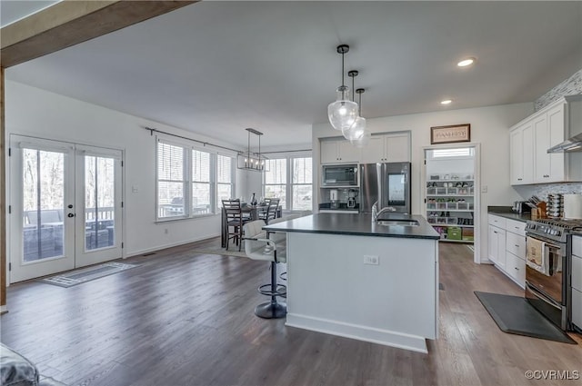 kitchen with a center island with sink, appliances with stainless steel finishes, dark hardwood / wood-style flooring, pendant lighting, and white cabinets