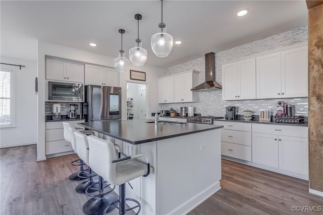 kitchen featuring appliances with stainless steel finishes, sink, white cabinets, a kitchen island with sink, and wall chimney range hood