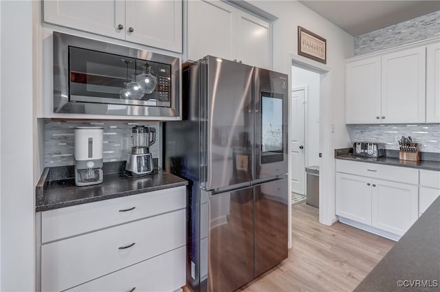 kitchen with decorative backsplash, light wood-type flooring, white cabinets, and appliances with stainless steel finishes