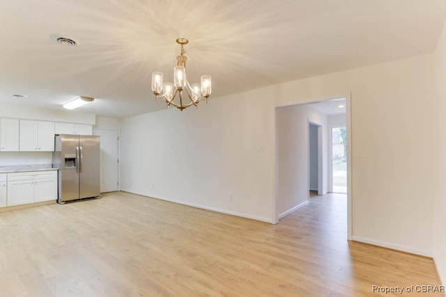 kitchen with light wood-type flooring, stainless steel fridge with ice dispenser, hanging light fixtures, and white cabinets