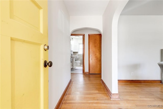 hallway featuring light wood-style floors, baseboards, and arched walkways