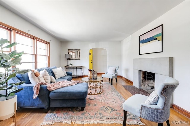 living room featuring a fireplace with flush hearth, arched walkways, baseboards, and wood finished floors