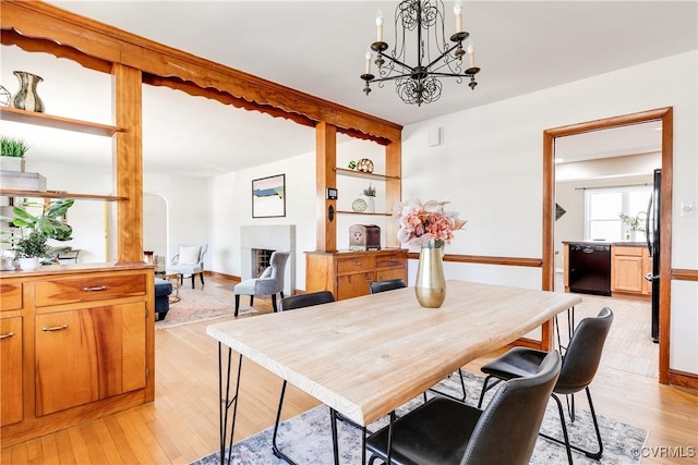 dining space with baseboards, a fireplace, light wood finished floors, and an inviting chandelier