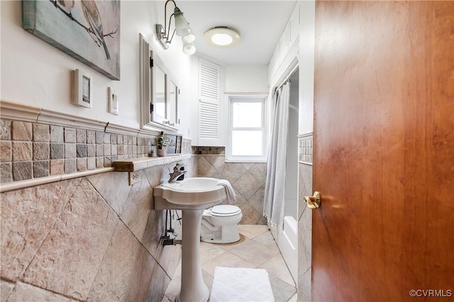 full bathroom featuring tile walls, a shower with curtain, toilet, wainscoting, and tile patterned flooring