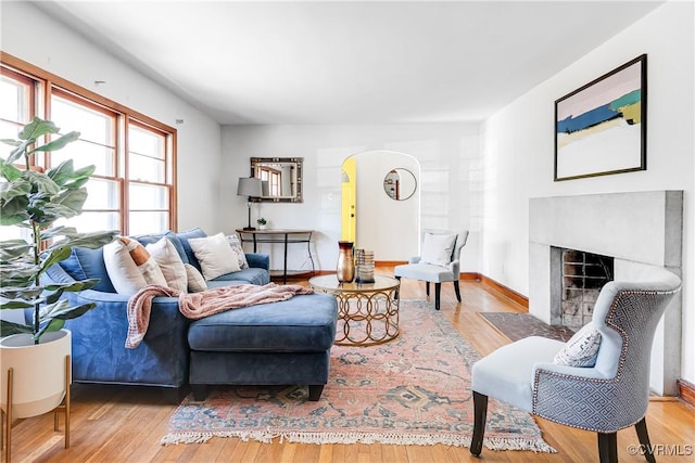 living area featuring a fireplace with flush hearth, arched walkways, baseboards, and hardwood / wood-style floors