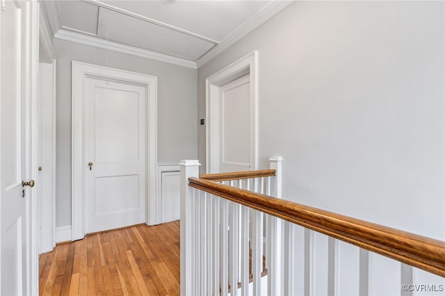 corridor featuring an upstairs landing, ornamental molding, light wood-style flooring, and attic access