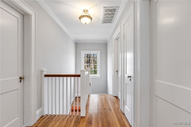 hallway with light wood-style floors, an upstairs landing, visible vents, and crown molding