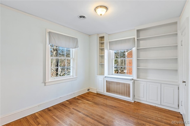 spare room featuring radiator, visible vents, plenty of natural light, and light wood finished floors