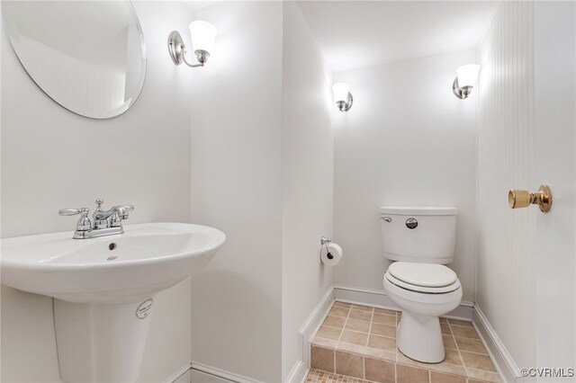 half bath with toilet, baseboards, and tile patterned floors