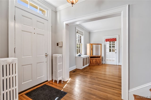 entryway with baseboards, ornamental molding, radiator heating unit, and light wood-style floors