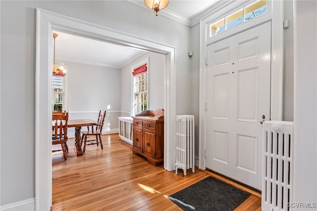 foyer with light wood-style floors, radiator, a notable chandelier, and crown molding