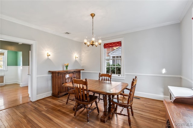 dining space with crown molding, visible vents, a chandelier, baseboards, and hardwood / wood-style flooring