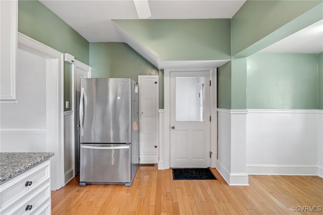 kitchen with light stone countertops, light wood-style flooring, white cabinetry, and freestanding refrigerator