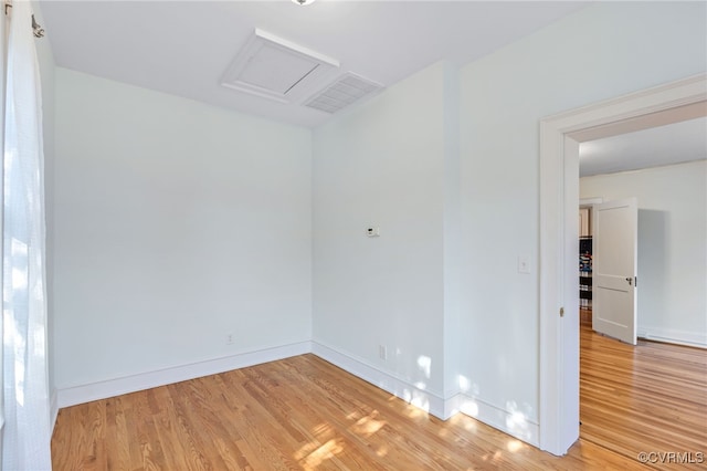 empty room featuring visible vents, light wood-type flooring, attic access, and baseboards