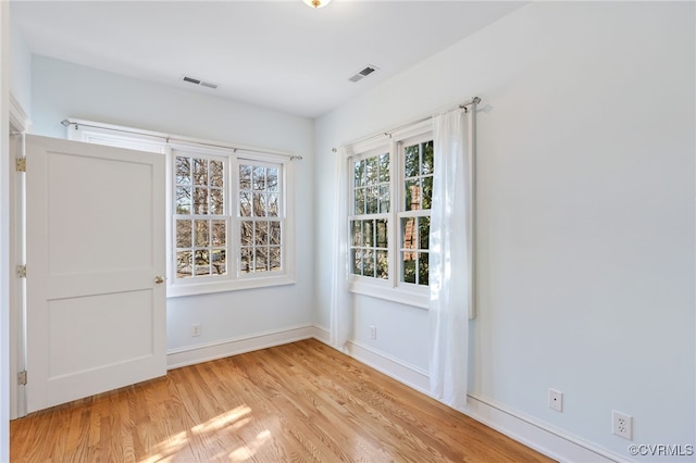 empty room with light wood finished floors, baseboards, and visible vents