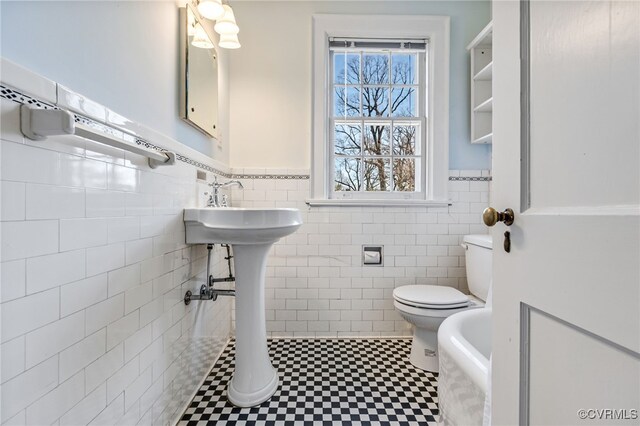 bathroom featuring toilet, a wainscoted wall, and tile walls