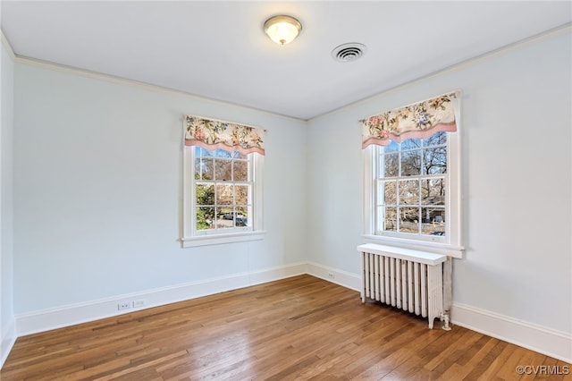 empty room featuring baseboards, visible vents, radiator heating unit, ornamental molding, and wood finished floors