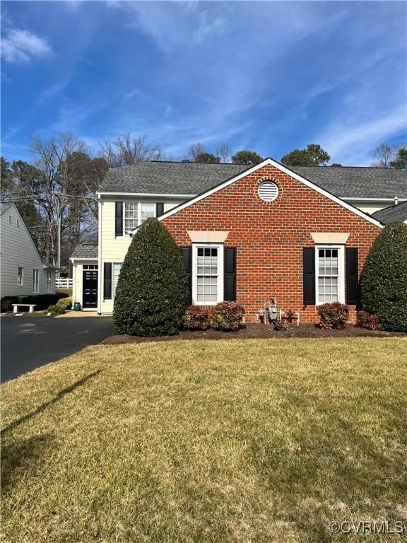 view of front of property featuring a shingled roof, a front lawn, and brick siding