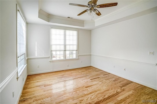 empty room with ornamental molding, a raised ceiling, and wood finished floors