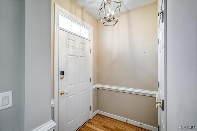 doorway to outside featuring a chandelier, light wood-type flooring, and baseboards