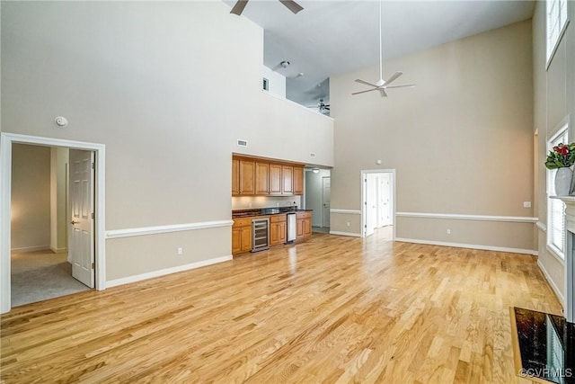 unfurnished living room featuring light wood-style floors, wine cooler, ceiling fan, and baseboards