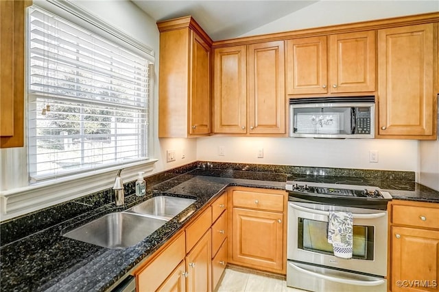 kitchen featuring lofted ceiling, appliances with stainless steel finishes, dark stone countertops, and a sink