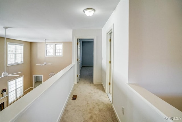 hallway with carpet, visible vents, baseboards, and an upstairs landing