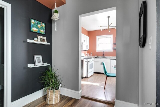 kitchen featuring hardwood / wood-style floors, sink, white cabinets, a chandelier, and white appliances