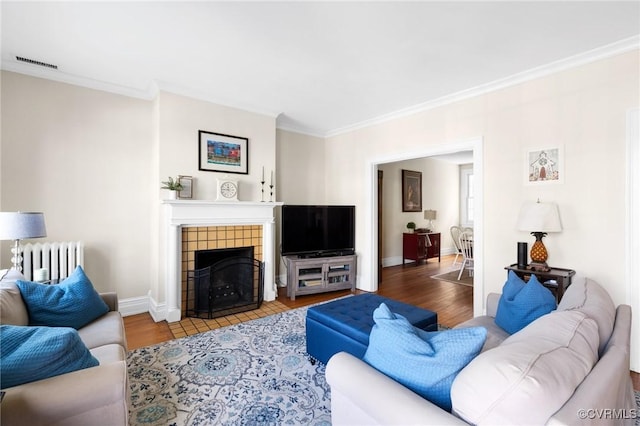 living room with radiator, a fireplace, visible vents, and wood finished floors