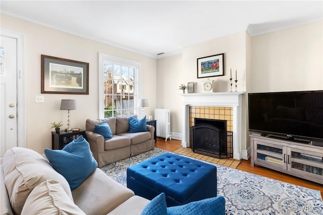 living area with light wood finished floors, baseboards, a tiled fireplace, radiator, and crown molding