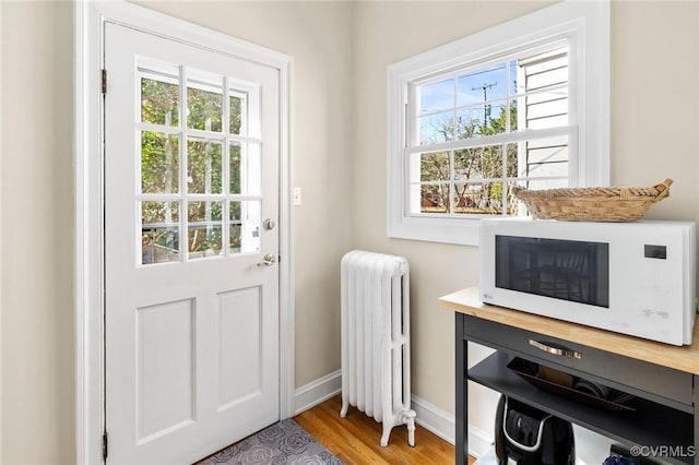 doorway featuring radiator heating unit, baseboards, and wood finished floors