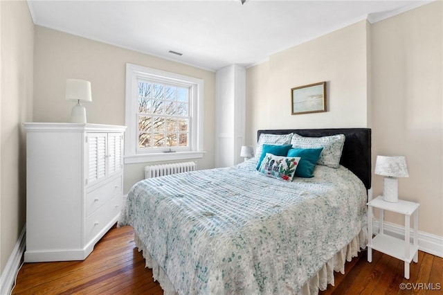 bedroom featuring radiator heating unit, wood-type flooring, visible vents, and baseboards