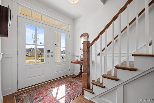 foyer entrance with french doors, a decorative wall, wainscoting, wood finished floors, and stairs