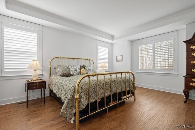 bedroom with a tray ceiling, ornamental molding, wood finished floors, and baseboards