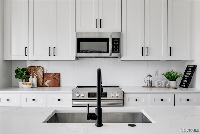 kitchen with white cabinetry, appliances with stainless steel finishes, light stone countertops, and decorative backsplash