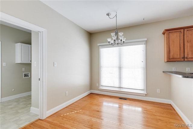 unfurnished dining area featuring light wood-style flooring, visible vents, baseboards, and a notable chandelier