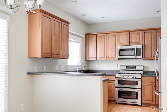 kitchen featuring dark countertops, appliances with stainless steel finishes, brown cabinets, a sink, and a notable chandelier