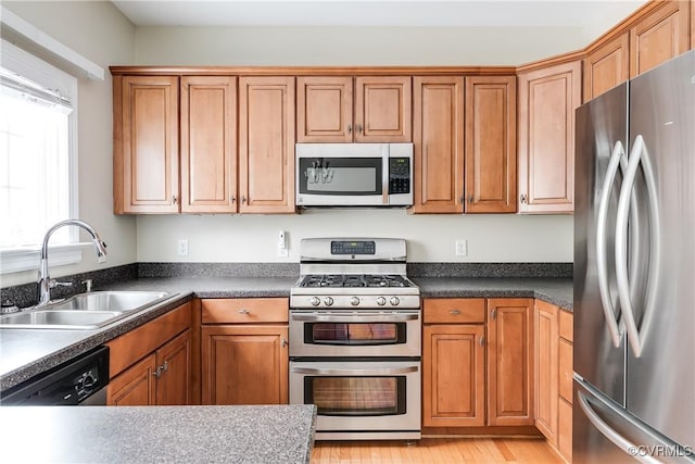 kitchen featuring dark countertops, appliances with stainless steel finishes, brown cabinets, and a sink