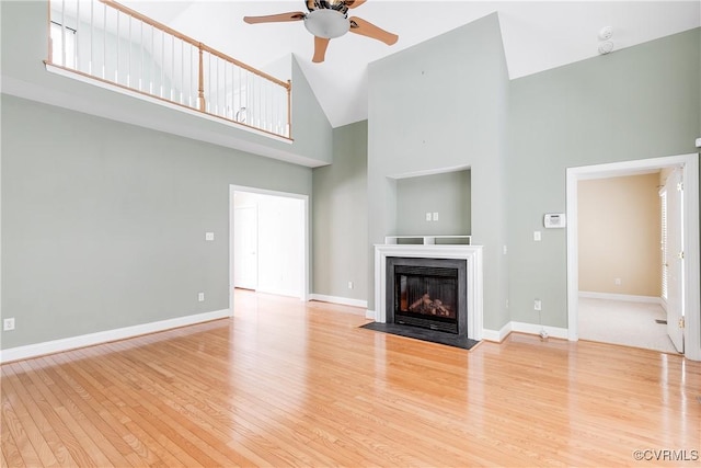 unfurnished living room featuring a fireplace with flush hearth, baseboards, light wood-style flooring, and a high ceiling