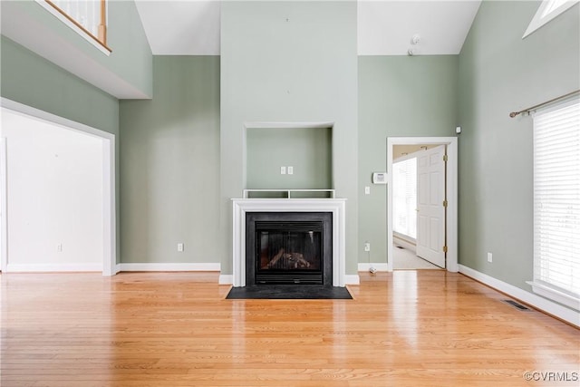 unfurnished living room featuring a towering ceiling, light wood-style flooring, and a wealth of natural light